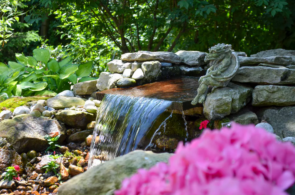 Close view of a natural stone waterfall with a small dragon sculpture and pink flowering plants